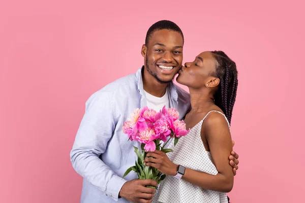 A woman holding flowers and kissing her boyfriend.