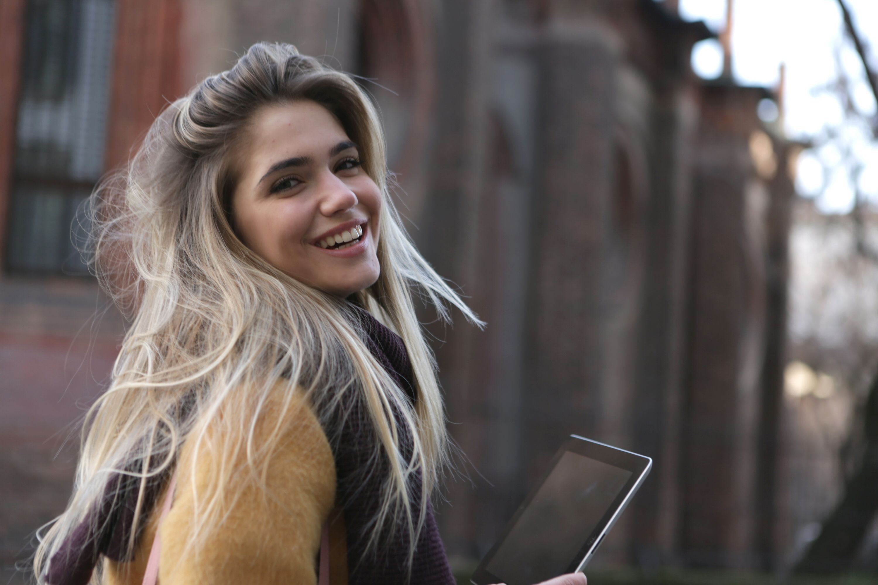 Smiling girl with tablet in hands, looking over shoulder, on the street.